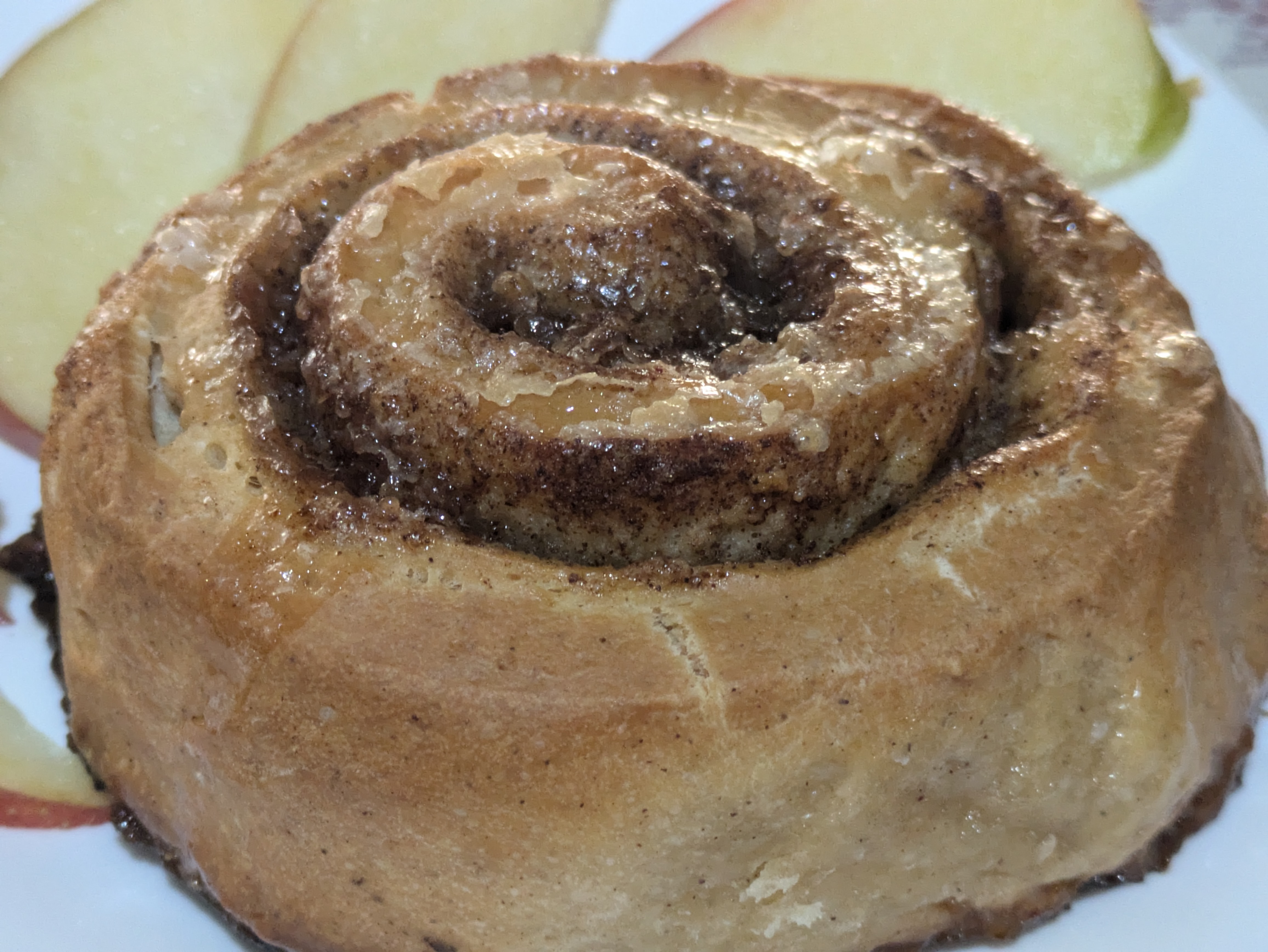 Cinnamon roll and apple slices on a white plater