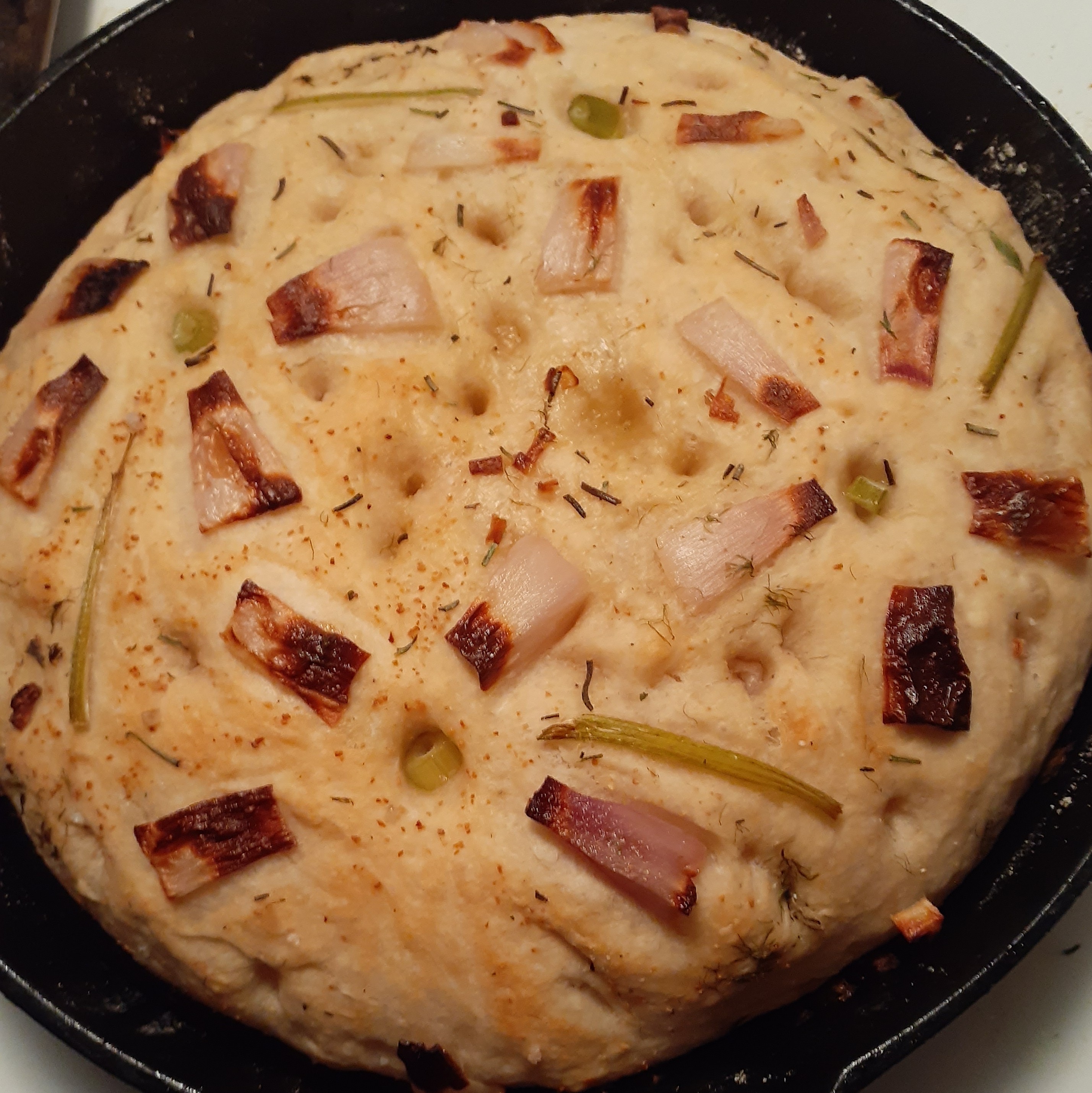 foccacia topped with red onions in floral design presented in cast iron pan